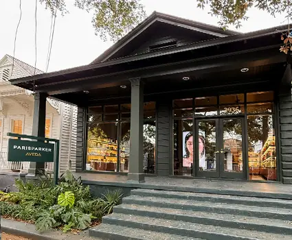 - Paris Parker Aveda Salons and Spas - Baton Rouge, New Orleans, Mandeville, LA Exterior of a dark-painted hair salon with large windows, steps leading to the entrance, and a "Paris Parker Aveda" sign in front. - Paris Parker Aveda Salons and Spas - Baton Rouge, New Orleans, Mandeville, LA