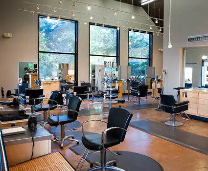 - Paris Parker Aveda Salons and Spas - Baton Rouge, New Orleans, Mandeville, LA Modern Aveda salon with black chairs, large mirrors, wooden stations, and tall windows letting in natural light. The space is clean and well-organized—perfect for your next haircut or balayage appointment. No people are present. - Paris Parker Aveda Salons and Spas - Baton Rouge, New Orleans, Mandeville, LA