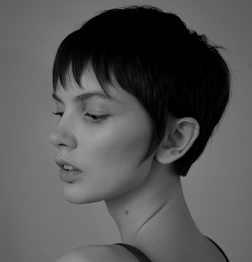 - Paris Parker Aveda Salons and Spas - Baton Rouge, New Orleans, Mandeville, LA Black and white portrait of a person with a fresh haircut and short dark hair, highlighting distinct facial features, looking to the left with a neutral expression against a plain background. - Paris Parker Aveda Salons and Spas - Baton Rouge, New Orleans, Mandeville, LA
