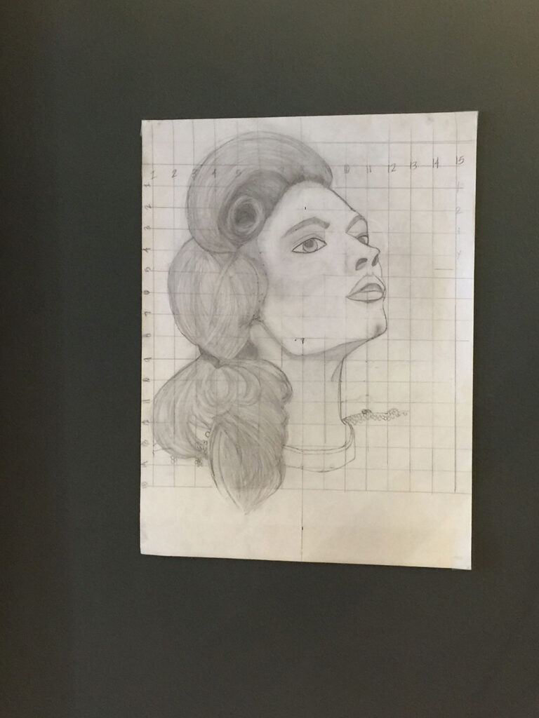 - Paris Parker Aveda Salons and Spas - Baton Rouge, New Orleans, Mandeville, LA Pencil portrait of a woman with wavy hair and an upturned gaze, highlighting her delicate facial features, drawn on grid paper and displayed against a dark background. - Paris Parker Aveda Salons and Spas - Baton Rouge, New Orleans, Mandeville, LA