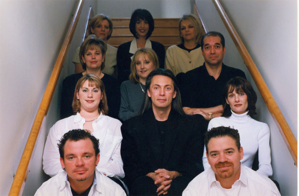 - Paris Parker Aveda Salons and Spas - Baton Rouge, New Orleans, Mandeville, LA A group of ten people, five men and five women, sit and stand on wooden stairs in two rows, facing the camera in a hair salon hallway. - Paris Parker Aveda Salons and Spas - Baton Rouge, New Orleans, Mandeville, LA