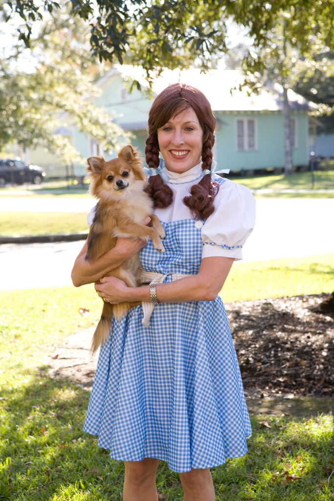 - Paris Parker Aveda Salons and Spas - Baton Rouge, New Orleans, Mandeville, LA A woman in a blue gingham dress and brown wig with braids stands outside holding a small brown dog, looking ready for a fresh haircut at the local Aveda Salon. - Paris Parker Aveda Salons and Spas - Baton Rouge, New Orleans, Mandeville, LA