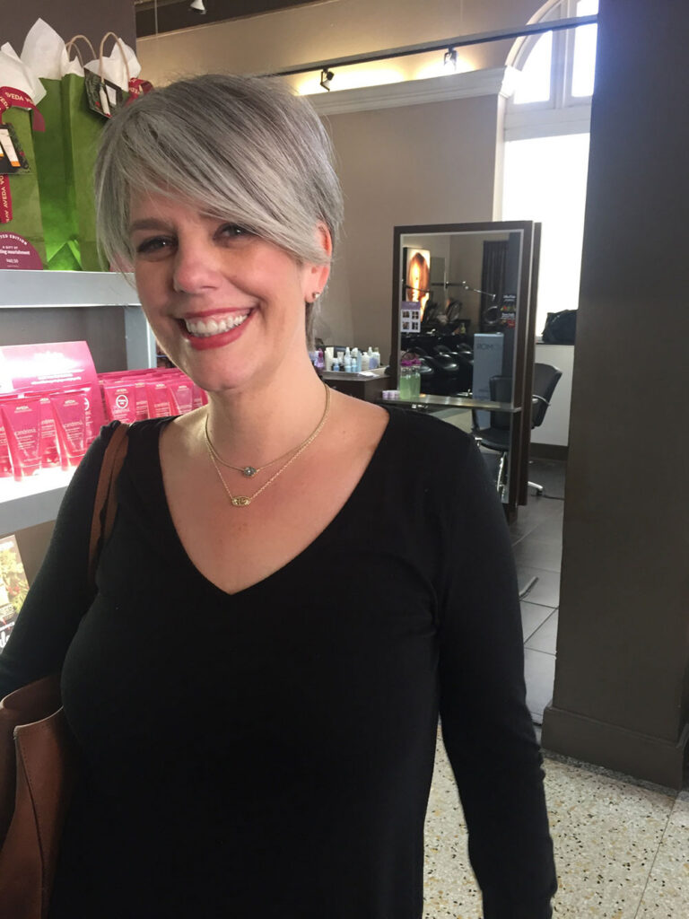 - Paris Parker Aveda Salons and Spas - Baton Rouge, New Orleans, Mandeville, LA Smiling person with short gray hair and a black top stands in a salon, surrounded by shelves of hair products and a styling station—ready for a fresh haircut or relaxing facial at this welcoming day spa. - Paris Parker Aveda Salons and Spas - Baton Rouge, New Orleans, Mandeville, LA