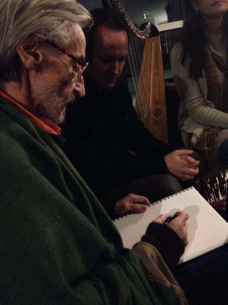- Paris Parker Aveda Salons and Spas - Baton Rouge, New Orleans, Mandeville, LA An older man with glasses sketches on a notepad while two others sit nearby, one partially visible and the other leaning forward as if waiting for their turn at a relaxing facial or balayage treatment at the day spa. - Paris Parker Aveda Salons and Spas - Baton Rouge, New Orleans, Mandeville, LA