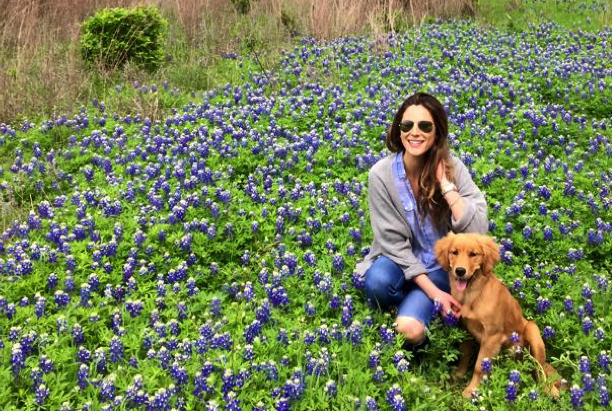 - Paris Parker Aveda Salons and Spas - Baton Rouge, New Orleans, Mandeville, LA Woman wearing sunglasses sits in a field of blue and purple wildflowers with a golden retriever puppy, enjoying a peaceful day reminiscent of visiting a tranquil day spa. - Paris Parker Aveda Salons and Spas - Baton Rouge, New Orleans, Mandeville, LA