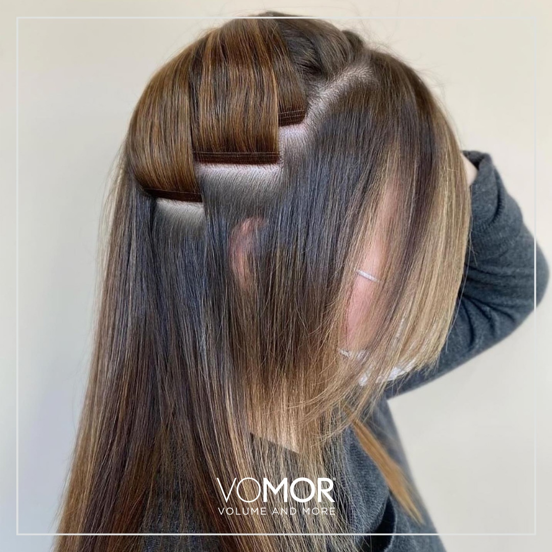 - Paris Parker Aveda Salons and Spas - Baton Rouge, New Orleans, Mandeville, LA Close-up of a person’s head showing hair extension installation with visible wefts and sectioned natural hair at an Aveda Salon, labeled "VOMOR Volume and More. - Paris Parker Aveda Salons and Spas - Baton Rouge, New Orleans, Mandeville, LA