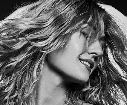 - Paris Parker Aveda Salons and Spas - Baton Rouge, New Orleans, Mandeville, LA Black and white photo of a woman with wavy hair, eyes closed, head tilted in bliss, and a slight smile, suggesting movement—capturing the fresh confidence after a new haircut. - Paris Parker Aveda Salons and Spas - Baton Rouge, New Orleans, Mandeville, LA