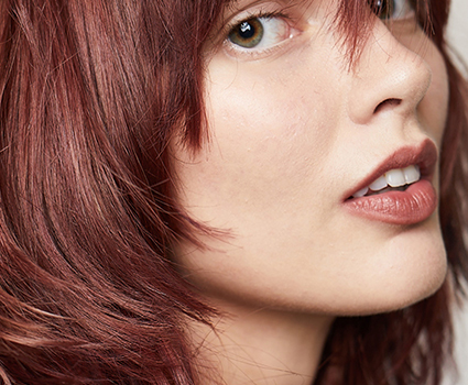 - Paris Parker Aveda Salons and Spas - Baton Rouge, New Orleans, Mandeville, LA Close-up of a person with a fresh Aveda Salon haircut—reddish-brown, layered hair, natural makeup, and a partially visible eye, looking slightly to the side. - Paris Parker Aveda Salons and Spas - Baton Rouge, New Orleans, Mandeville, LA