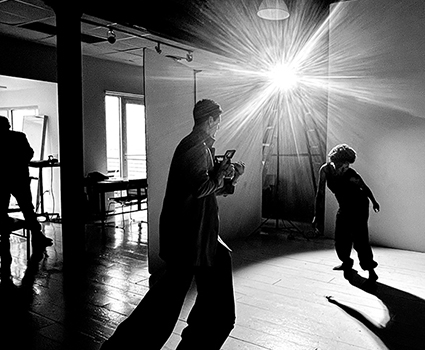 - Paris Parker Aveda Salons and Spas - Baton Rouge, New Orleans, Mandeville, LA Three people are in a room with a bright light source; one holds a camera, another stands near the light as if showcasing a balayage, and a third person is partially visible on the left. - Paris Parker Aveda Salons and Spas - Baton Rouge, New Orleans, Mandeville, LA