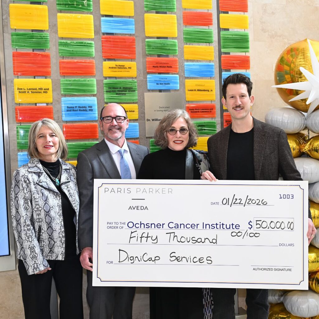 - Paris Parker Aveda Salons and Spas - Baton Rouge, New Orleans, Mandeville, LA Four people pose indoors holding a large ceremonial check for $50,000 made out to Ochsner Cancer Institute for DigniCap Services. Colorful plaques and an Aveda Salon Day Spa sign are displayed on the wall behind them. - Paris Parker Aveda Salons and Spas - Baton Rouge, New Orleans, Mandeville, LA