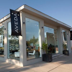 - Paris Parker Aveda Salons and Spas - Baton Rouge, New Orleans, Mandeville, LA Modern storefront with large glass windows, a black Aveda Salon banner, and potted plants at the entrance on a sunny day—a welcoming spot for your next haircut. - Paris Parker Aveda Salons and Spas - Baton Rouge, New Orleans, Mandeville, LA