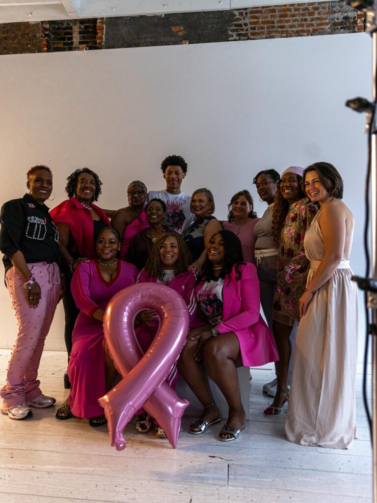 - Paris Parker Aveda Salons and Spas - Baton Rouge, New Orleans, Mandeville, LA A group of people pose indoors at an Aveda Salon, many wearing pink and some holding a large pink ribbon balloon, symbolizing support for breast cancer awareness. - Paris Parker Aveda Salons and Spas - Baton Rouge, New Orleans, Mandeville, LA