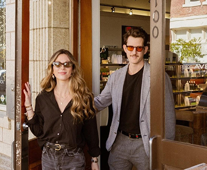 - Paris Parker Aveda Salons and Spas - Baton Rouge, New Orleans, Mandeville, LA A woman and a man wearing sunglasses are walking out of a hair salon, with the man holding the door open. Shelves with products are visible inside the shop. - Paris Parker Aveda Salons and Spas - Baton Rouge, New Orleans, Mandeville, LA
